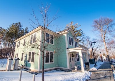 Exterior snapshot of the Youth and Family Services building that houses PUCK in the town of Bennington, Vermont. Photo description: A large mint green building illuminated by sunshine. The building has off-white trim. Snow is on the ground outside the two-story building and the trees are bare.