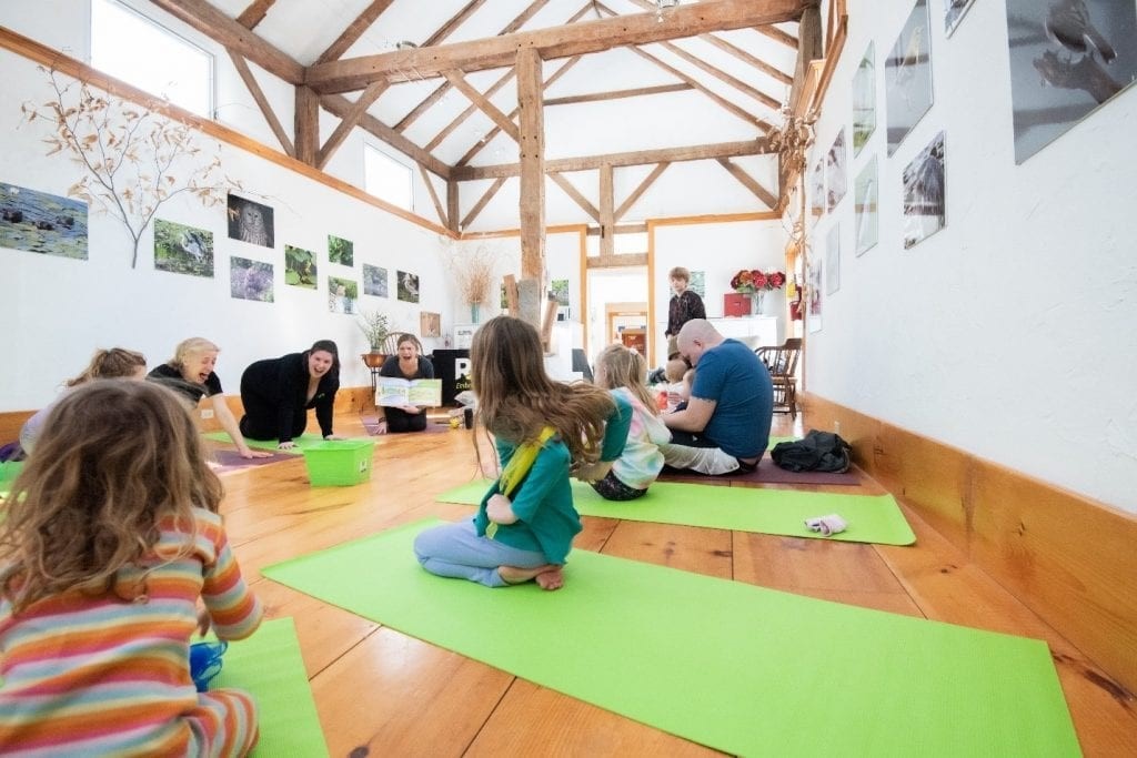 Children sit on green yoga mats with their parents and program manager, Elisha Underwood, in an open room.